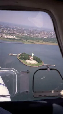 The Statue of Liberty seen out the left side of
                        a light aircraft banking around it.