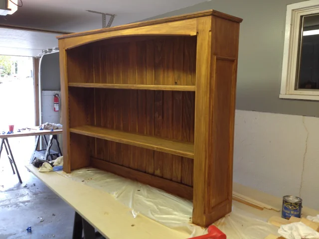 The finished stained wooden hutch top with arched
                      trim and two long shelves, standing in the
                      workshop.