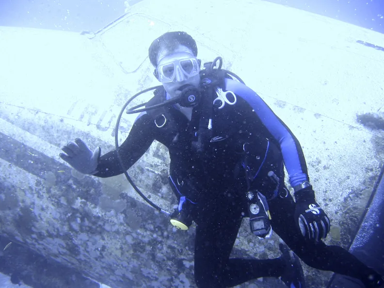 A scuba diver beside the fuselage of a sunken
                      airplane underwater.