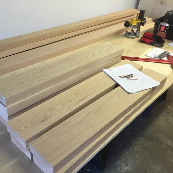 Milled oak boards and a cut-list sketch on a
                      workbench with a router and layout tools.