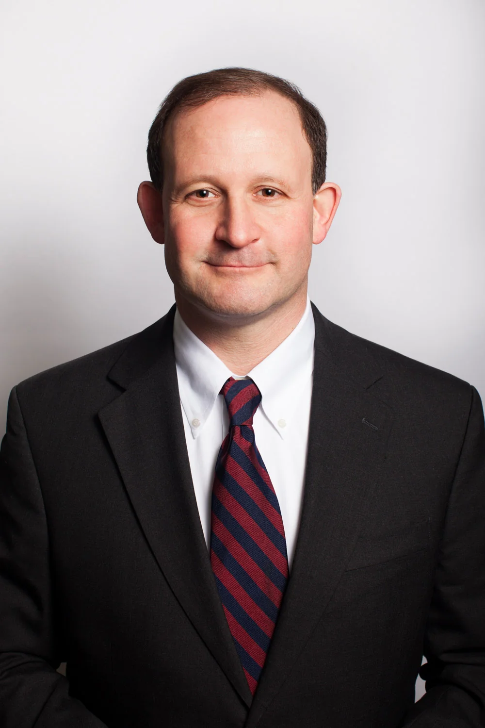 Scott Germaise in a dark suit, white shirt, and
                    red-and-navy striped tie against a plain light
                    background.